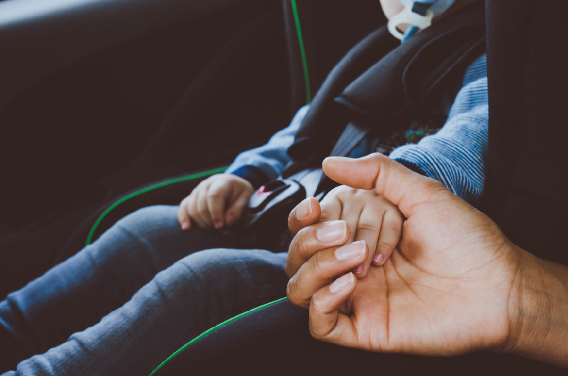 dziecko w foteliku samochodowym trzymające rodzica za rękę