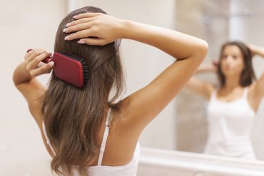 Kobieta przed lustrem czesząca włosy szczotką