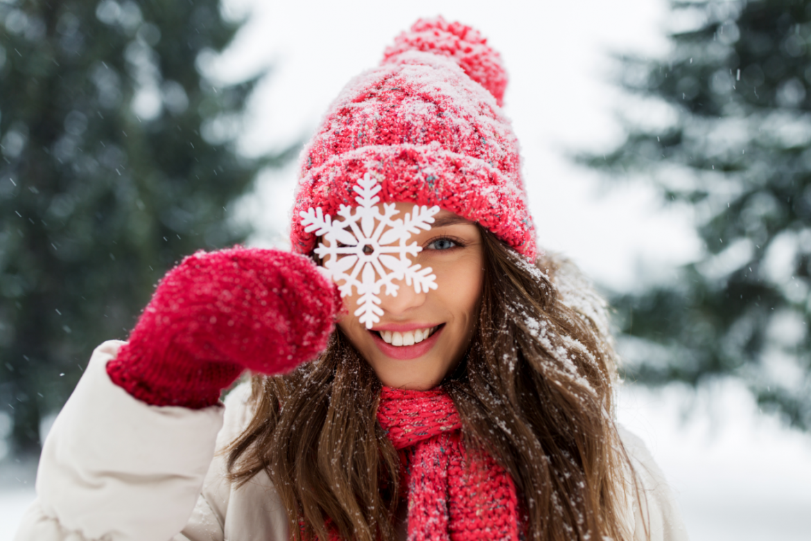 Kobieta w czerwonej czapce, szaliku i rękawiczkach na tle zimowego krajobrazu i z płatkiem śniegu przy twarzy