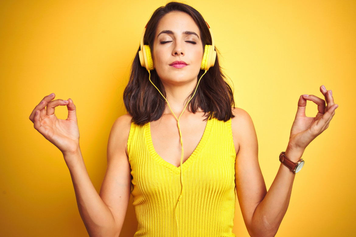 Piękna kobieta w żółtym swetrze z żółtymi słuchawkami na uszach słucha muzyki i relaksuje się