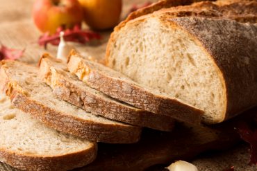 Pokrojony świeży chleb w kompozycji z jesiennymi liśćmi i czosnkiem.